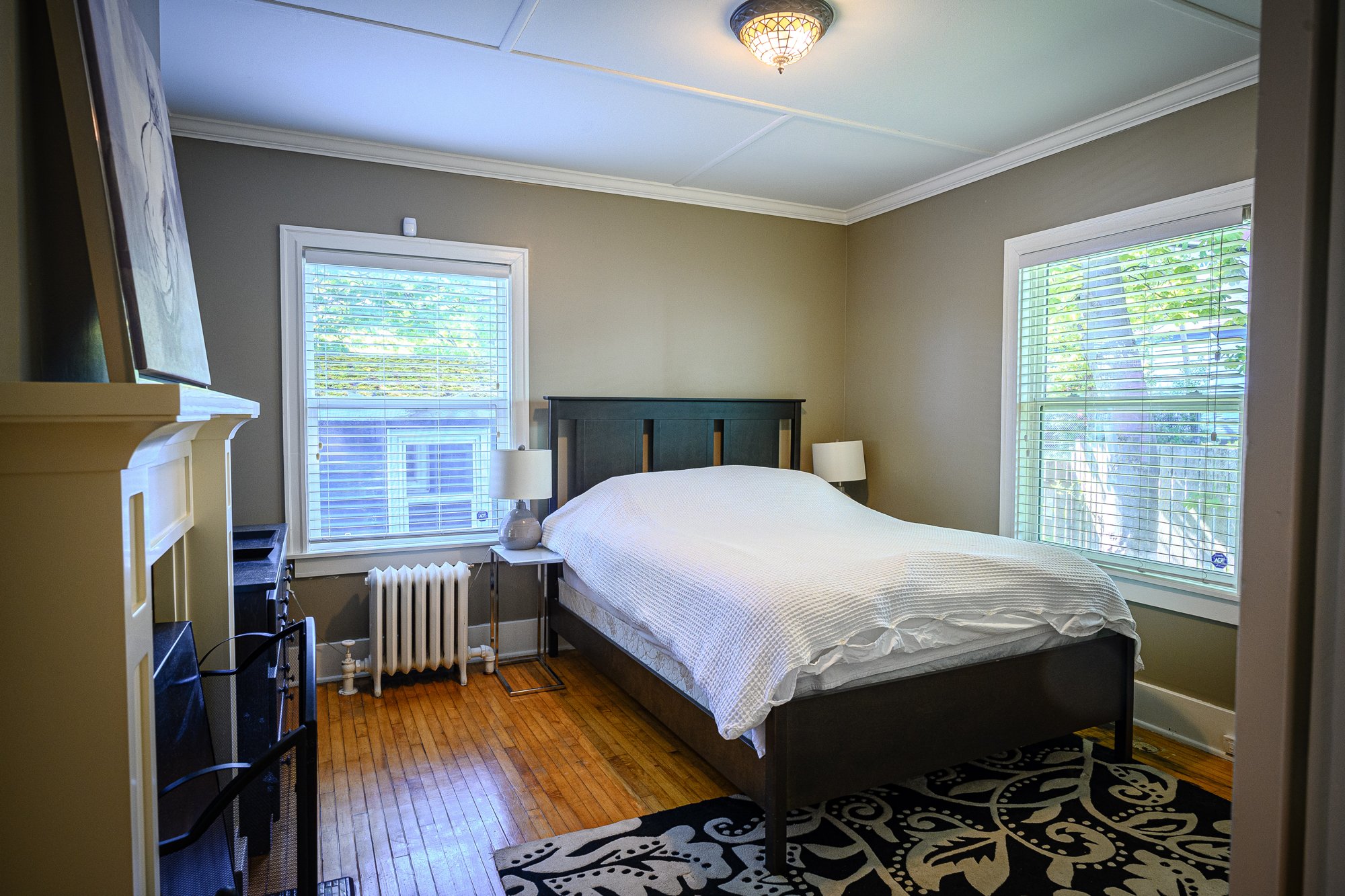 Bright bedroom with white bedding, two windows and a dark wood headboard