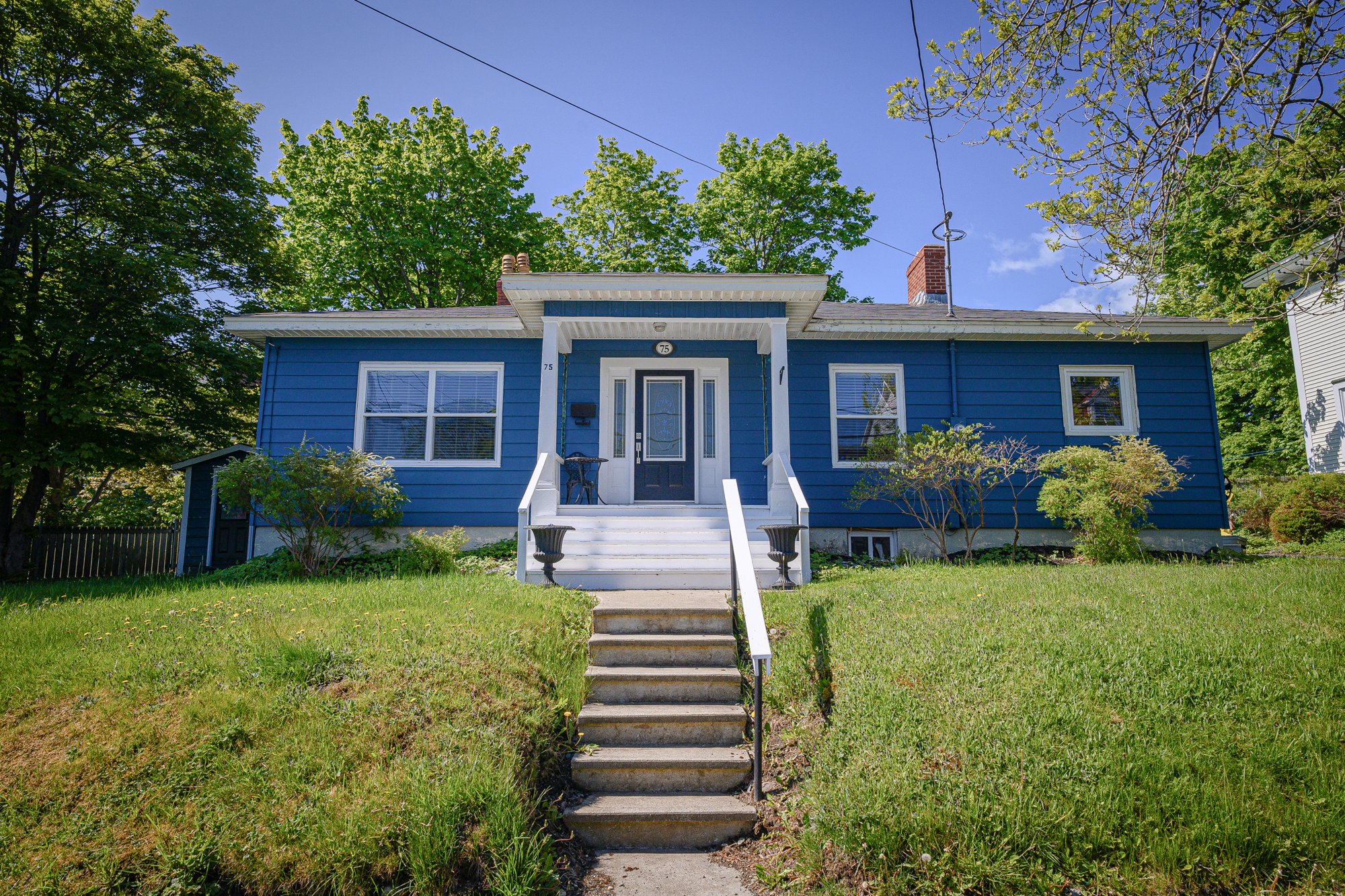 Blue bungalow with a white front porch and landscaped front garden